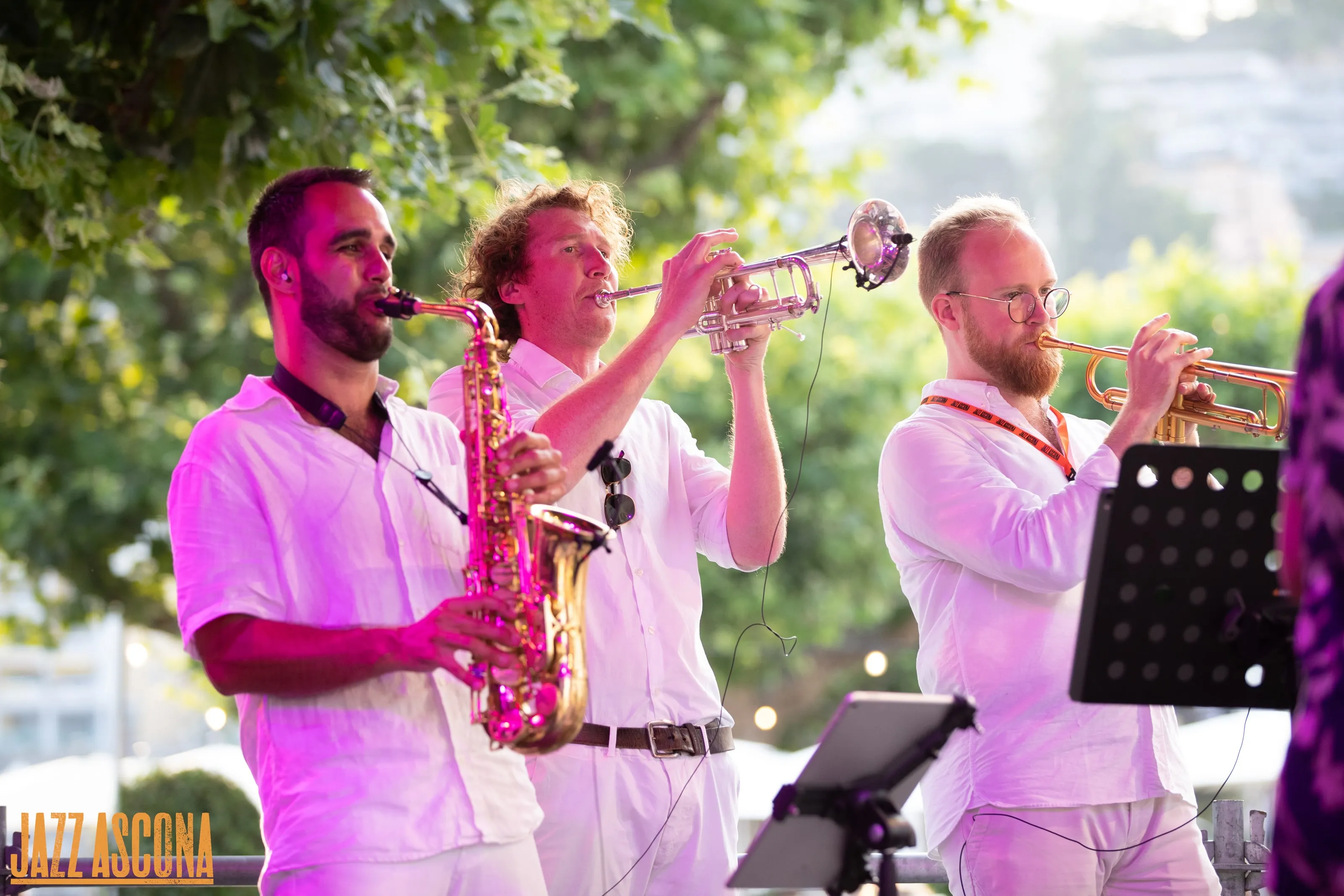 Saxophone et deux trompettes en chemises blanches jouent en plein air dans la lumière dorée du soir, à JazzAscona
