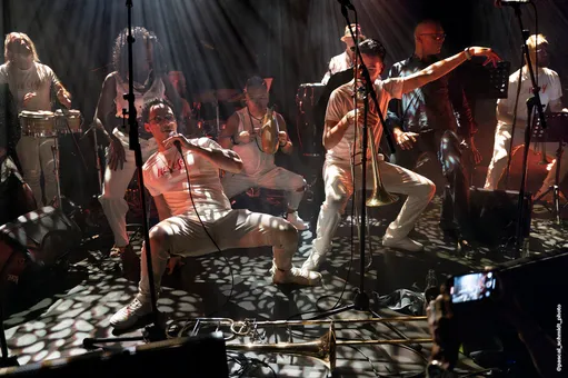 Chanteur et tromboniste descendent dans la danse au club Les Jumeaux, sous une lumière tachetée — © Pascal Schmidt