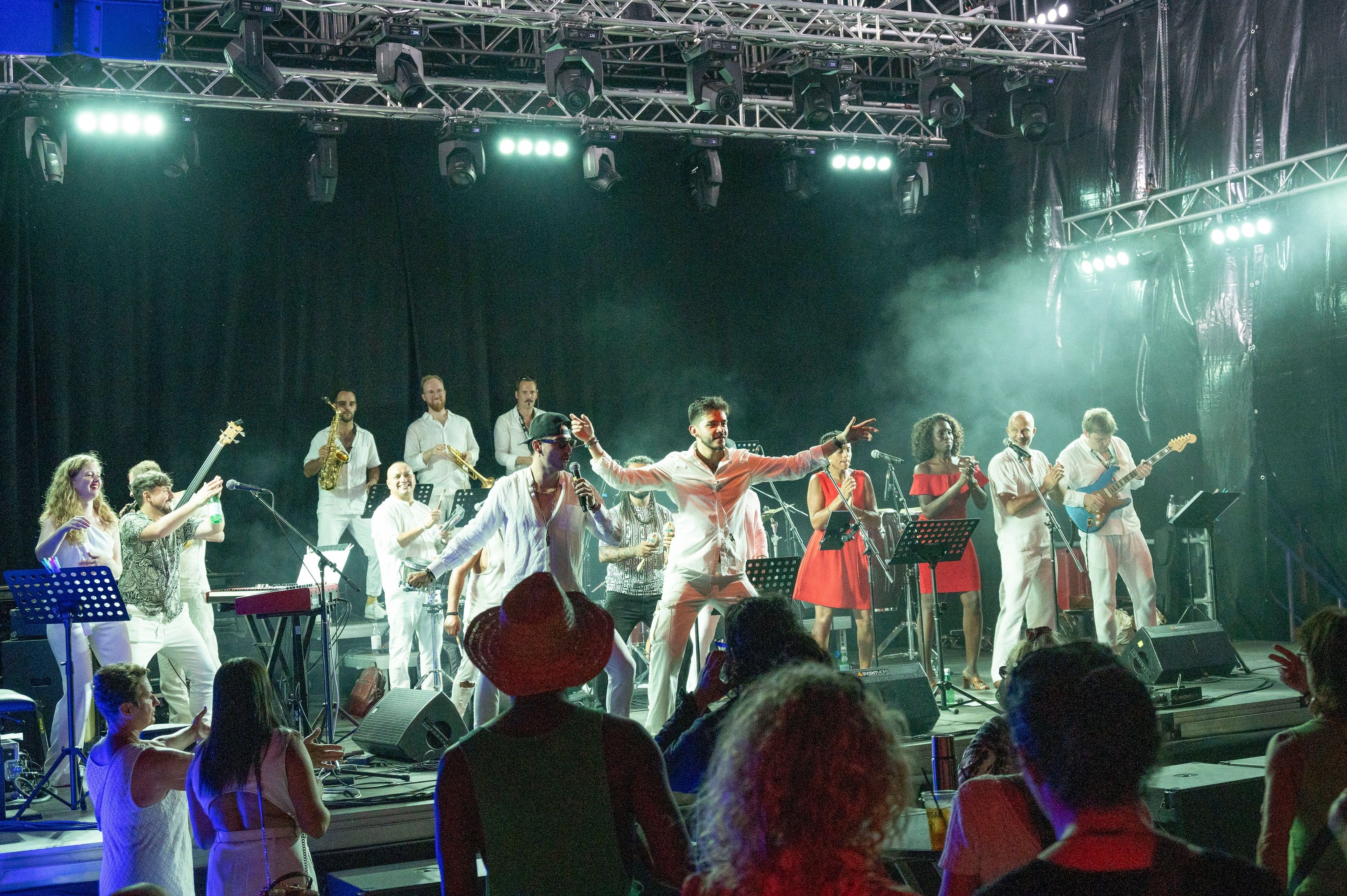 L'orchestre au complet en blanc sur la grande scène, les chanteuses en rouge dans la fumée et les lumières, le public danse au premier plan